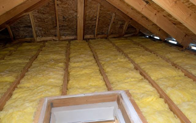 Yellow batts filling an attic floor around the framed opening of the attic hatch
