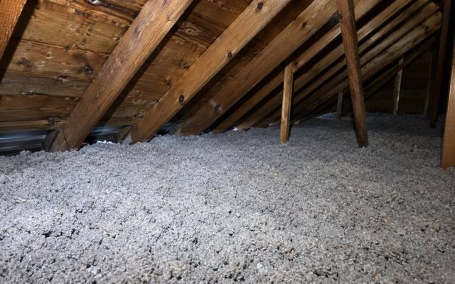 Deep grey loose fill spread across an attic floor under dark wooden rafters
