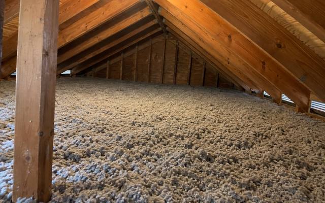 Thick blown cellulose covering an attic floor around a wooden post beneath the roof boards