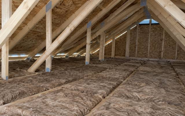 Rows of brown batt insulation across an attic floor beneath pale wood trusses